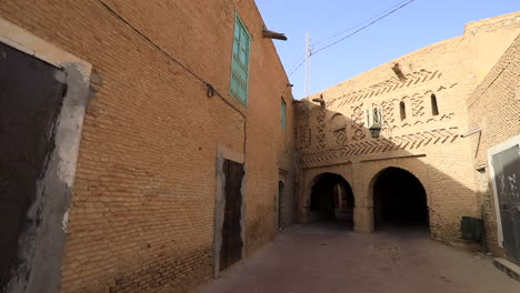 Narrow-alley-in-Sbeitla-with-traditional-brick-architecture,-blue-sky