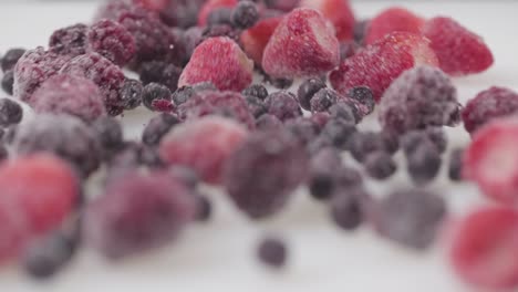 Bayas-De-Frambuesa-Rojas-Y-Negras-Congeladas-Rodando-Sobre-Una-Superficie-Blanca-Cerca-De-Frutas-Naturales-Orgánicas-Saludables