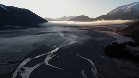 flying-over-a-braided-river-in-Arthurs-Pass-in-a-valley-surrounded-by-mountains-at-sunrise-in-New-Zealand