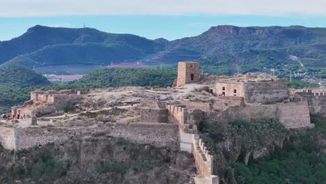 Vuelo-Con-Un-Dron-Con-Efecto-Paralaje-Sobre-La-Parte-Más-Alta-De-La-Fortaleza-Donde-Hay-Gente-Visitándola-Con-Un-Hermoso-Fondo-De-Montañas-Y-Un-Cielo-Azul-En-Una-Mañana-Valencia-España