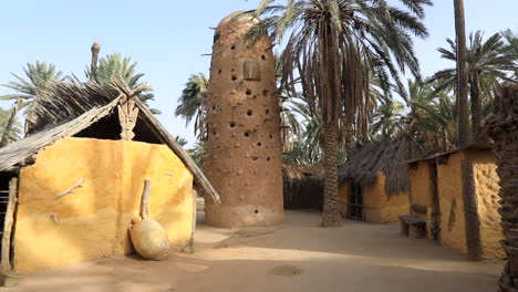 Traditionelle-Gebäude-Aus-Lehmziegeln-Der-Sahara-Mit-Einem-Einzigartigen-Getreideturm-Zwischen-Palmen