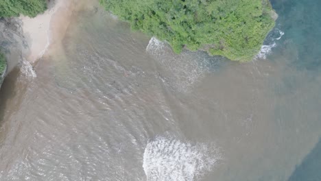 Top-down-aerial-drone-shot-over-polluted-sewage-water-and-floating-trash-with-debris-over-dead-coral-reef-mixing-with-turquoise-water-and-tropical-coastine-in-Bali-Indonesia