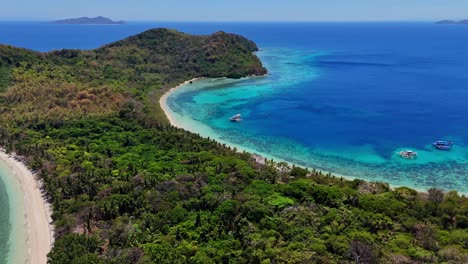 Drone-footage-of-a-tropical-island-with-jungle,-beach-and-boats-near-Palawan-in-the-Philippines
