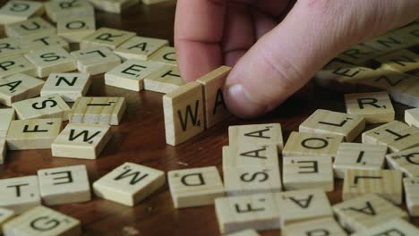 Right-hand-places-Scrabble-tile-letters-on-table-to-form-word-WAR