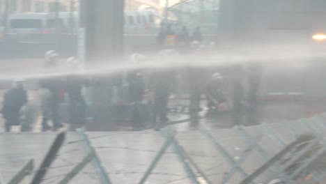 Belgian-riot-police-officer-spraying-with-water-hose-during-manifestation-in-front-of-the-European-Parliament-building-in-Brussels,-Belgium