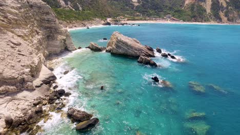 Retreating-drone-shot-of-the-rocky-beachfront-of-Petanoi,-an-isolated-resort-located-in-Kefalonia-in-the-West-Coast-of-Greece