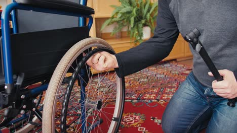 A-man-in-jeans-and-a-black-and-gray-T-shirt-checks-the-amount-of-air-in-the-tires-of-a-wheelchair