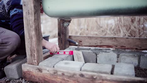 The-Man-is-Employing-a-Level-to-Guarantee-that-the-Concrete-Block-is-Properly-Aligned-Beneath-the-DIY-Hot-Tub---Close-Up