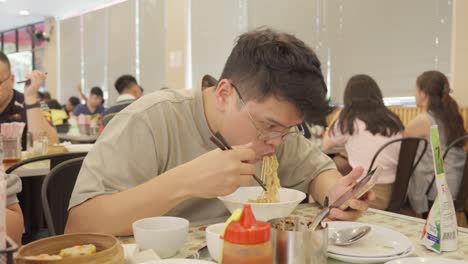 Caballero-Asiático-Con-Gafas-Saboreando-Un-Plato-De-Fideos-En-Un-Restaurante