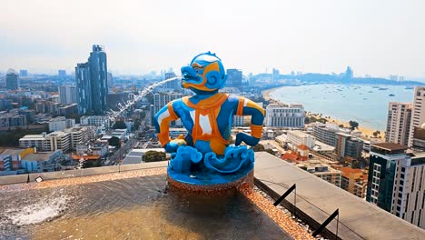 Vibrant-rooftop-statue-overlooking-Pattaya-cityscape-and-bay,-sunny-day