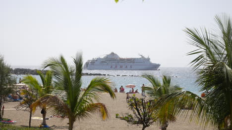 A-ferry-cruise-liner-boat-docked-at-a-busy-seaside-beach-in-los-christianos-in-tenerife