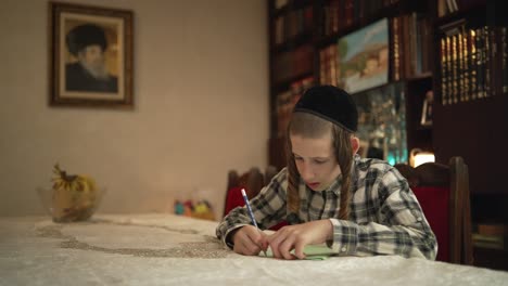 A-jewish-12-year-old-boy-is-sitting-down-by-a-table-and-writing