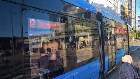 Central-Oslo-Public-Transportation,-Norway,-Tram-Passing-Intersection-Between-Downtown-Buildings-on-Sunny-Day