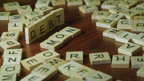Words-DEBT-and-MONEY-formed-with-game-tile-letters,-DEBT-falls-over