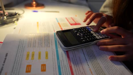 Closeup-of-slender-female-fingers-using-calculator-as-she-studies-late-at-night-under-desk-lamp-light