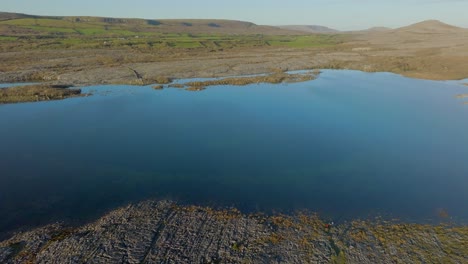 High-angle-orbit-around-waters-edge-where-blue-sky-reflects-dissapearing-to-sharp-limestone-rock-formations-in-the-Burren-Ireland