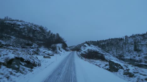 Schneebedeckte-Straße-In-Norwegen-Mit-Einer-Drohne,-Die-Sich-In-Der-Dämmerung-Schnell-Auf-Ein-Auto-Zubewegt