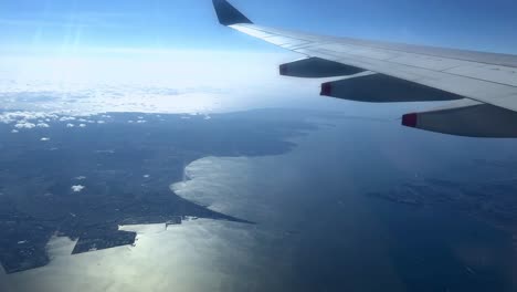 Luftaufnahme-Aus-Dem-Flugzeugfenster,-Flügel-über-Der-Küste-Mit-Blauem-Himmel