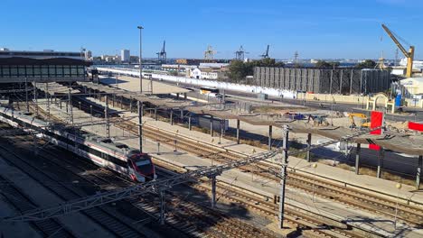 Train-on-Railway-Leaving-Cadiz-Spain-Station,-Harbor-Cranes-in-Background