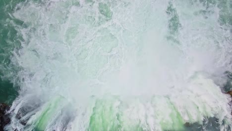 Static-top-down-aerial-shot-of-wide-waterfall-gushing-into-river-in-Iceland