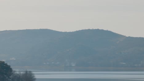 A-pan-left-tripod-movement-of-a-small-town-landscape,-transition-over-the-lake,-clear-water,-sunny-weather,-green-forest-trees-on-the-mountain,-red-rooftops,-European-buildings,-4K-video-close-up-shot