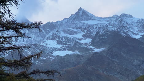 Schweizer-Alpen-Herbst-Erster-Schnee-Bestäubung-Berggipfel-Saas-Fee-Zermatt-Saastal-Alpin-Tal-Chalet-Skiort-Stadt-Sonnenuntergang-Orange-Rosa-Hohe-Wolken-Schweiz-Europa-Lerche-Baum-Wind-Filmisch-Rutsche-Links-