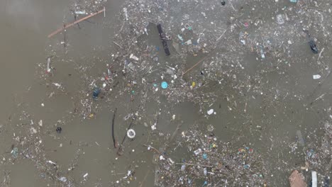 Low-altitude-aerial-drone-shot-over-polluted-muddy-sewage-ocean-water-and-floating-trash-with-debris-in-Bali-Indonesia