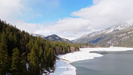 Gorgeous-drone-view-of-Lake-Kachess-with-snow-bank-and-evergreen-forest-in-Washington-State