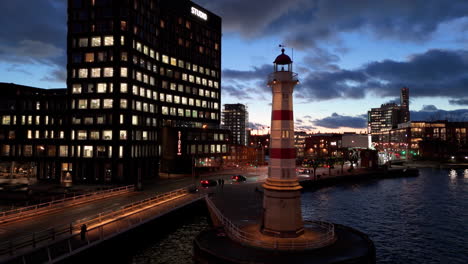 Malmo-Old-Lighthouse-on-waterfront-with-illuminated-buildings,-night-aerial