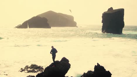 Man-silhouette-standing-on-rock-with-open-arms-against-monsteiros-beach-in-Sao-Miguel,-Azores-Island