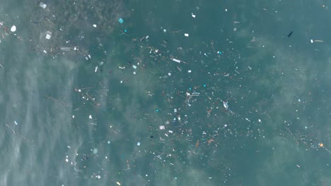 Top-down-drone-shot-of-polluted-water-filled-with-plastic-trash-and-dead-coral-reef-in-the-turqouise-tropical-water-of-Balangan-Beach-Uluwatu-Bali-Indonesia