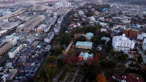 A-bustling-cityscape-at-dusk-with-a-park,-capturing-the-transition-from-day-to-night,-aerial-view