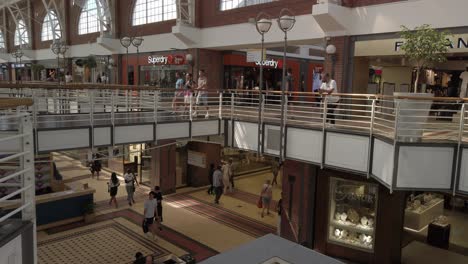 People,-Tourists-walk-inside-shopping-mall-modern-stores-cape-town-south-Africa,-pale-brown-tones-two-floored-building