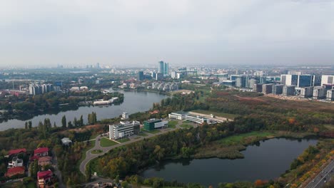 Aerial-view-of-Bucharest-suburbs-with-lake,-autumn-foliage,-and-modern-buildings