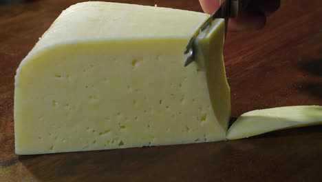 Reichhaltiger-Holländischer-Gouda-Käse,-In-Scheiben-Geschnitten-Mit-Messer-Auf-Dunklem-Schneidebrett