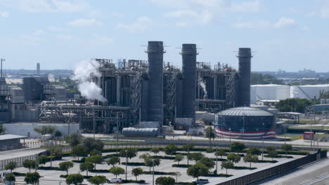 Contempla-Una-Enorme-Planta-De-Gas-Natural-De-Energía-Limpia-Con-Humo-Blanco-Ondulante,-Frente-A-La-Bandera-De-Estados-Unidos-Ondeando-En-El-Fondo-Del-Video,-Que-Representa-Prácticas-De-Energía-Sostenible-Y-Patriotismo.