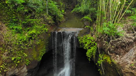 Remote-waterfall-flowing-into-pond-surrounded-by-lush-green-vegetation-in-Ubud,-Bali-in-Indonesia