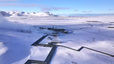 A-geothermal-power-plant-in-a-snowy-icelandic-landscape,-steam-rising,-clear-blue-sky,-aerial-view