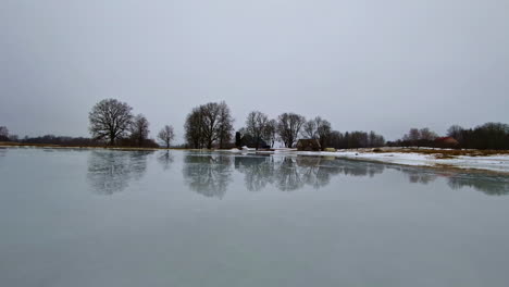 Snow-and-ice-pond-on-a-gray-day---panorama-with-trees-reflecting-off-the-lake's-surface