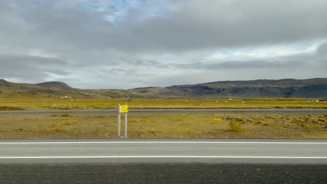 Green-fields-and-mountains-in-cloudy-Iceland,-POV-from-car-on-highway