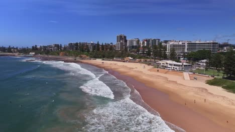 Aerial-reveal-of-surf-sand-and-beach-goers-enjoying-a-sunny-dat-at-North-Wollongong-Beach