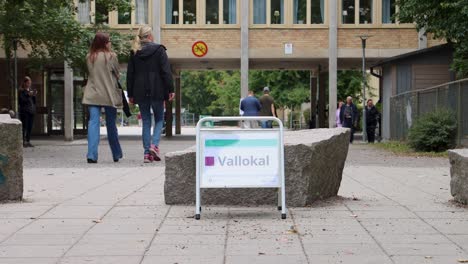 People-walk-by-polling-station-sign-on-election-day,-Stockholm,-Sweden