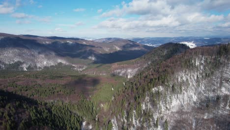Siriu-mountains-with-snowy-patches-and-lush-forests-under-a-blue-sky,-aerial-view