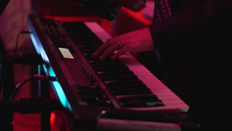 A-man-is-playing-a-keyboard-with-his-hands-during-a-party-in-dark-club-illuminated-with-colors-lights