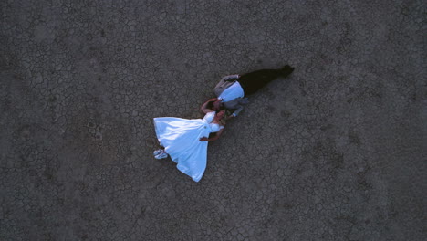 Top-Down-Aerial-View-of-Newlywed-Couple-Lying-on-Dry-Ground,-Wedding-Photoshoot
