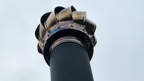 Looking-up-at-Stainless-steel-chimney-cap-spinning-on-top-of-metallic-stove-pipe-flue-in-the-breeze