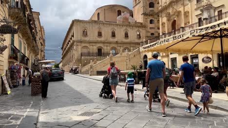 Street-view-tourists-walking-along-historic-street,-Noto,-Sicily