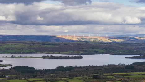 Timelapse-of-rural-nature-farmland-with-wind-turbines-in-hills-and-lake-in-distance-during-sunny-cloudy-day-viewed-from-Carrowkeel-in-county-Sligo-in-Ireland