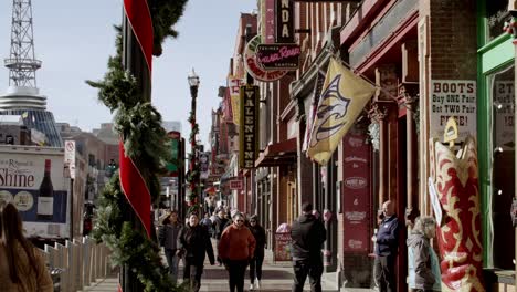 Tourists-on-Broadway-Street-in-Nashville,-Tennessee-during-the-day-with-video-tilting-up-in-slow-motion