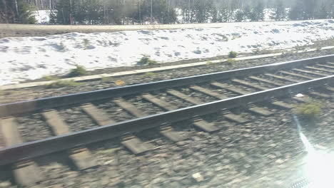 Railway-tracks-glistening-under-sunlight-with-remnants-of-snow,-captured-from-moving-train-in-Finland-from-Vuokatti-to-Rovaniemi